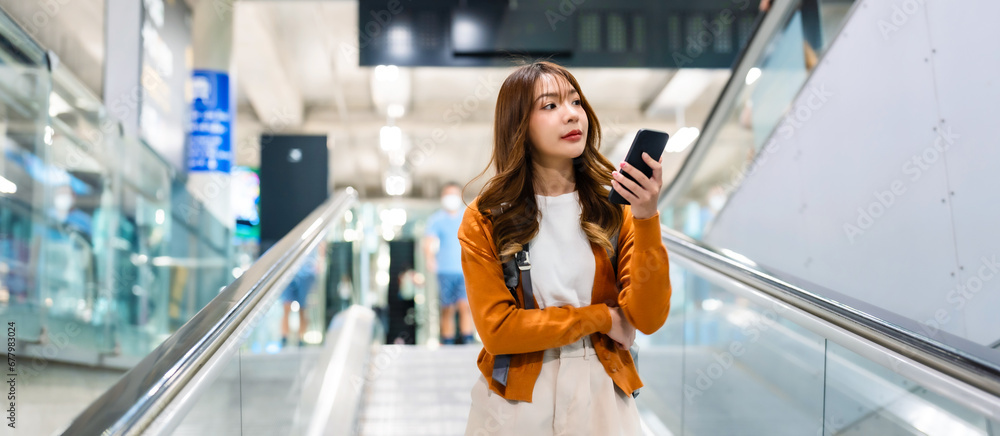 Young asian woman in international airport terminal or modern train station. Backpacker passenger female commuter walking on escalator - obrazy, fototapety, plakaty 