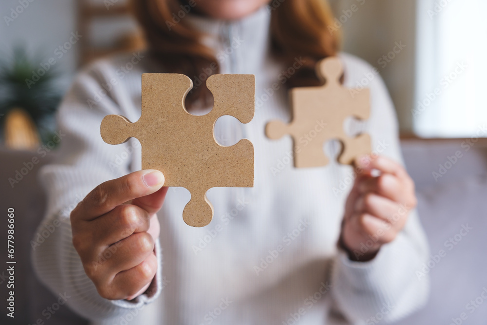 Closeup image of a woman holding and putting a piece of wooden jigsaw puzzle together Closeup image of a woman holding and putting a piece of wooden jigsaw puzzle together