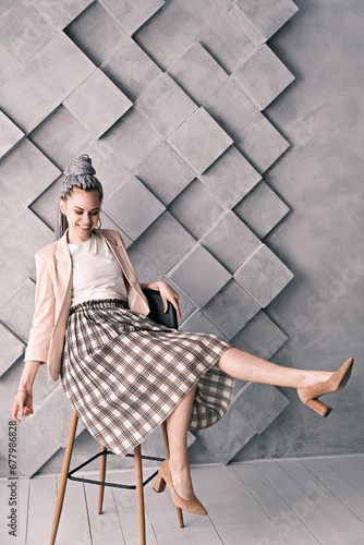 Attractive cheerful business woman with dreadlocks on her head sitting on a chair on a gray background.