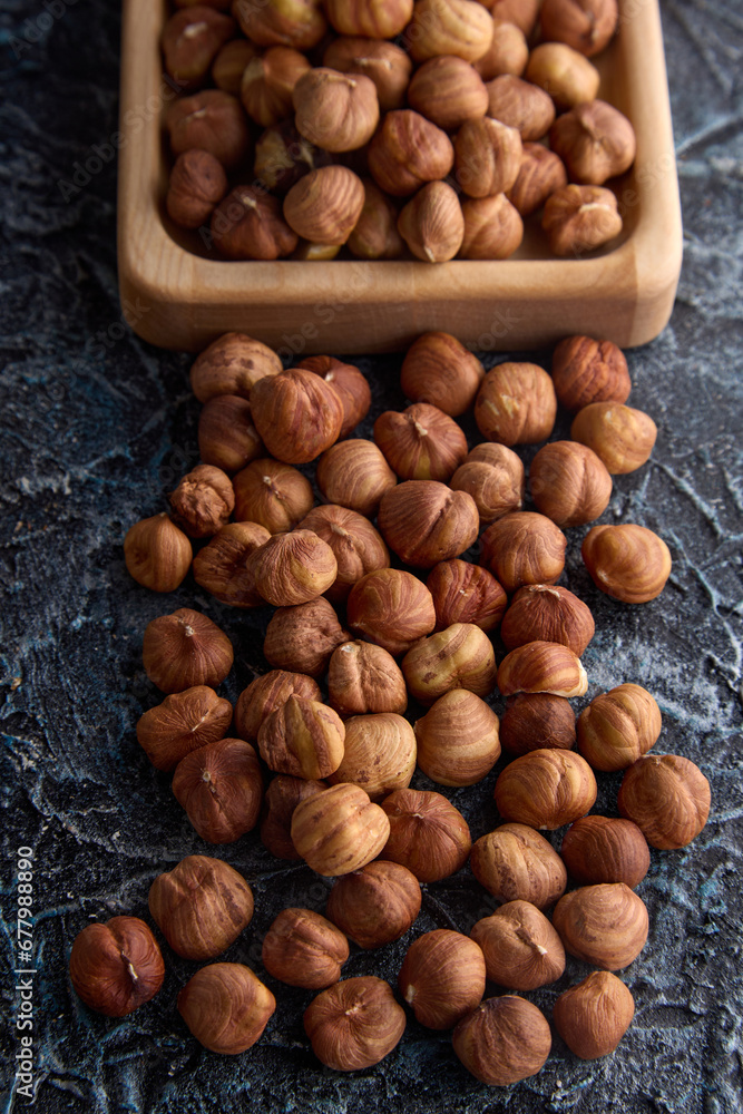 Top view of ripe hazelnuts randomly arranged on a textured gray background. Delicious roasted hazelnuts on the table and in a wooden bowl Top view of ripe hazelnuts randomly arranged on a textured gray background. Delicious roasted hazelnuts on the table and in a wooden bowl