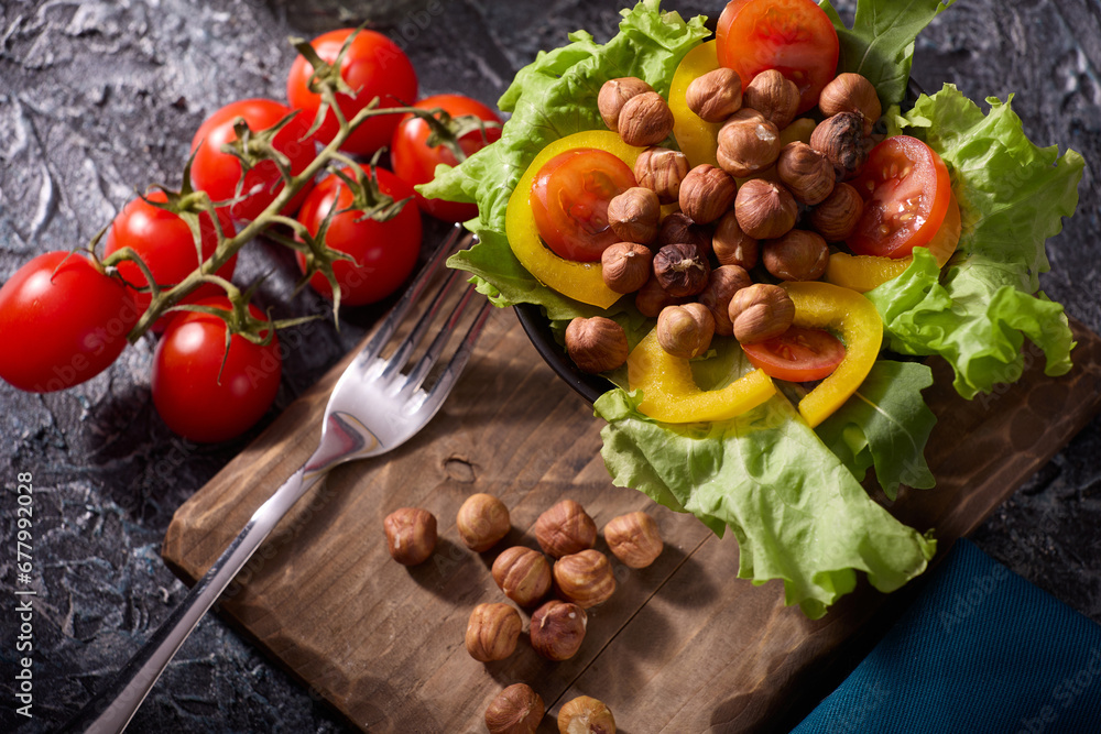 Top view of the slicing of fresh vegetables and hazelnuts, which lies in a plate on a wooden board. Salad of tomatoes, peppers and nuts, sprinkled with olive oil on a spectacular dark background.