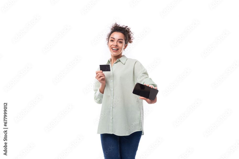 smiling young brunette curly woman dressed in a plaid shirt holding a credit card smartphone smiling young brunette curly woman dressed in a plaid shirt holding a credit card smartphone