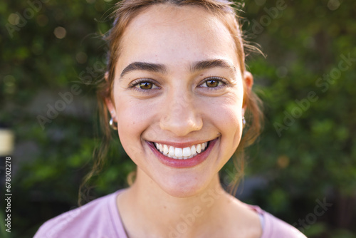 Portrait of happy biracial woman with long brown hair smiling in sunny garden