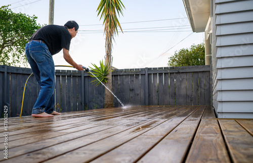 Man washing wooden deck with a water sprayer. Auckland. photo
