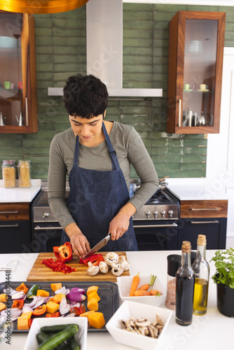 Happy biracial woman preparing food, chopping vegetables in kitchen at home, copy space