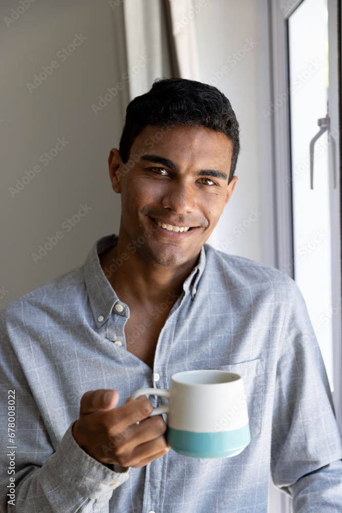 Portrait of happy biracial man holding mug next to window at home Portrait of happy biracial man holding mug next to window at home