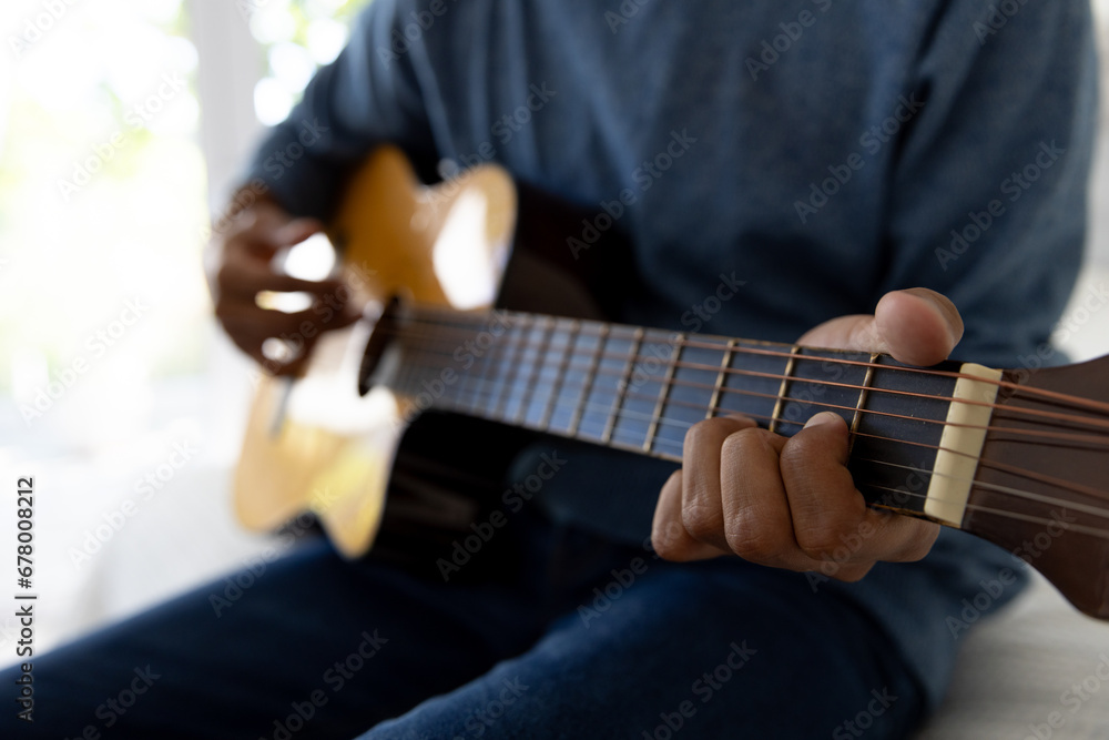 Midsection of biracial man sitting on bed playing guitar at home