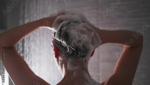 Woman massages foamy hair in shower cabin photo