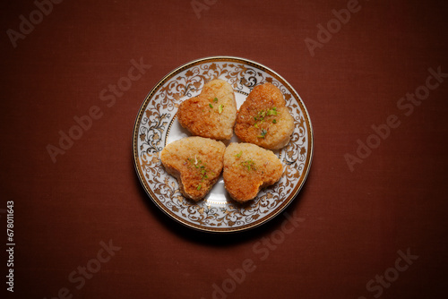 Top view of an Indian Traditional sweet called "Heart Shaped Milk Cake" an Indian Sweet made up of whole milk" served on a ceramic plate on a dark brown background.