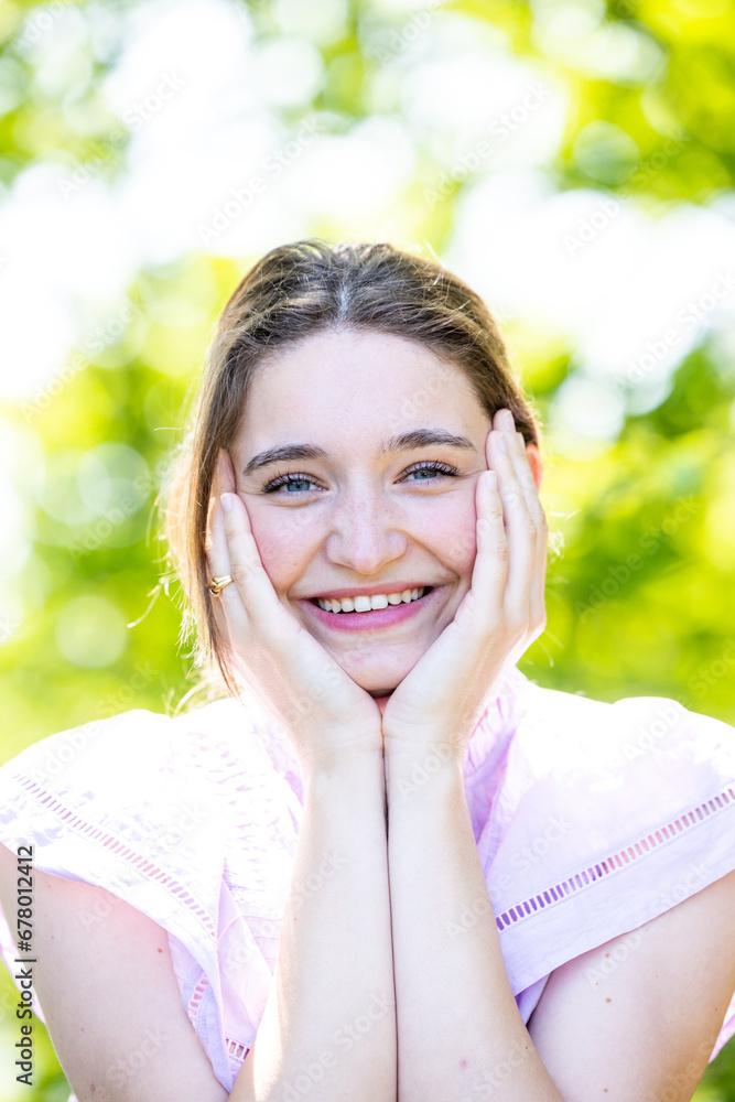 In this vibrant portrait, a young woman's laughter fills the frame, set against a natural green background. Her perfect skin and subtle makeup accentuate her genuine smile, embodying a lifestyle of