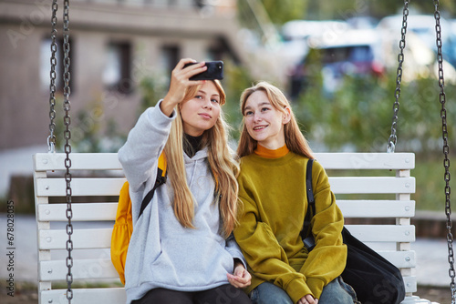 two teenage girls taking selfie  sitting on a swing © Cavan