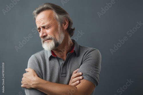People, healthcare and problem concept - unhappy man suffering from neck or shoulder pain at home. Mature bearded man has shoulder pain. with copy space for text. Man holding his injured shoulder photo