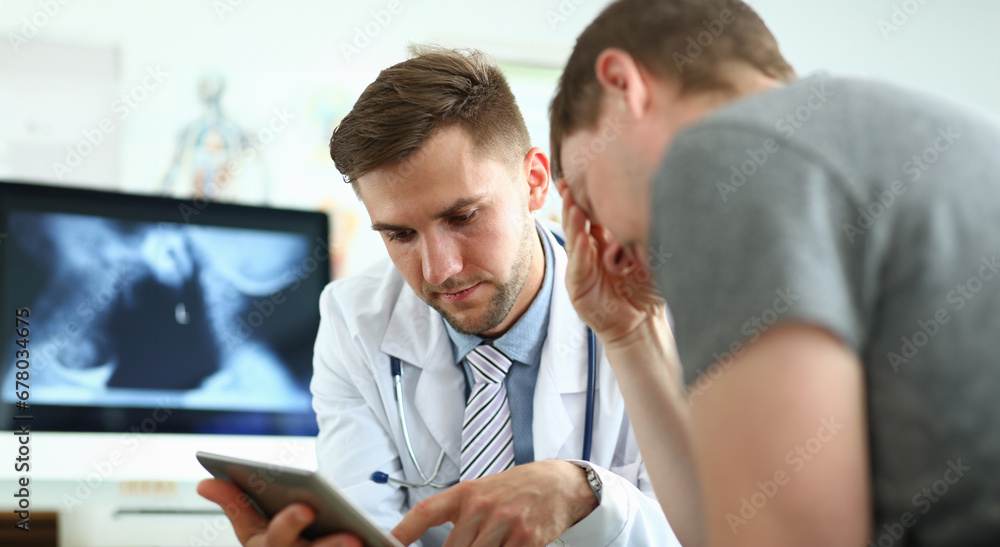 Portrait of serious doctor indicating bad diagnosis to sad and unsettling patient. Man explaining to visitor treatment method. Medicine and healthcare concept. Blurred background Portrait of serious doctor indicating bad diagnosis to sad and unsettling patient. Man explaining to visitor treatment method. Medicine and healthcare concept. Blurred background