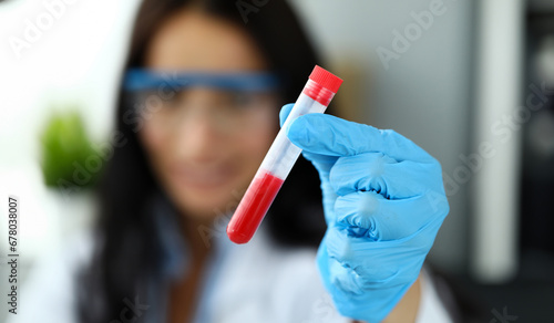 Female hand in blue protective gloves holding test tube with red liquid closeup