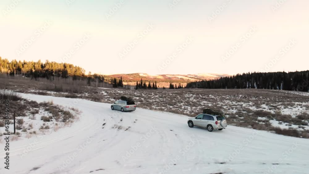 Aerial decent of cars driving in snow with Christmas trees in Idaho National Forest during a winter sunset. Aerial decent of cars driving in snow with Christmas trees in Idaho National Forest during a winter sunset.