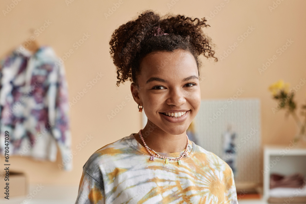 Fototapeta premium Happy young woman in tie dye t-shirt standing in front of camera in workshop, craft studio or atelier creating new stylish and trendy attire