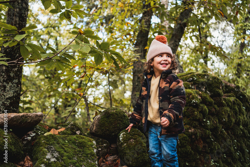 portrait of fashionable little boy with hat playing happily on a forest path while teaching his parents about plants