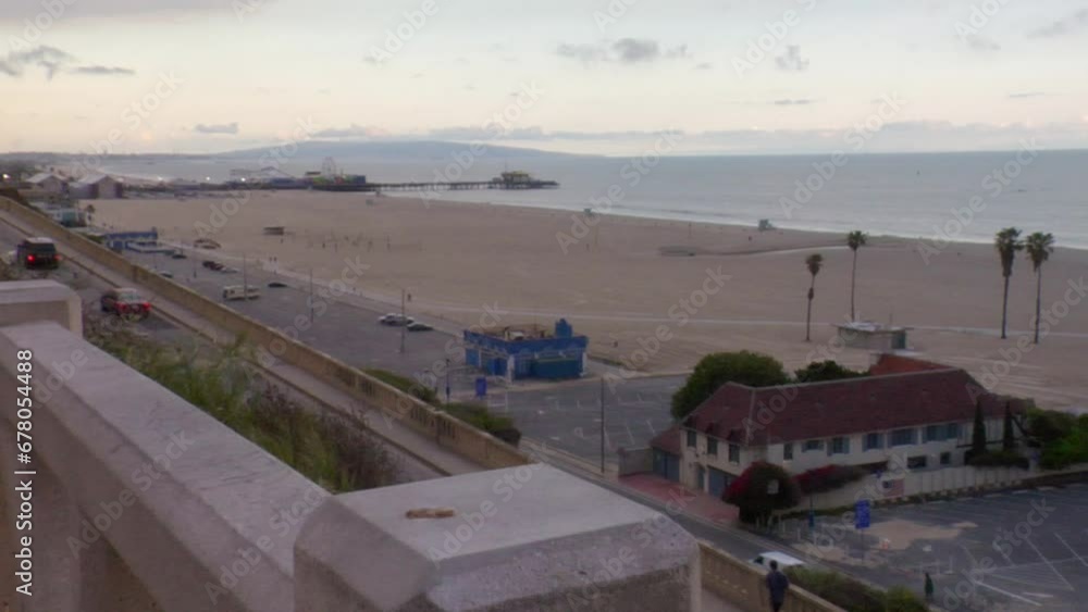 Steady zoom-in starting from a view of the California Incline, the Pacific Coast Highway, and Santa Monica Beach in the foreground, ending on a tight shot of the famous Santa Monica Pier Steady zoom-in starting from a view of the California Incline, the Pacific Coast Highway, and Santa Monica Beach in the foreground, ending on a tight shot of the famous Santa Monica Pier