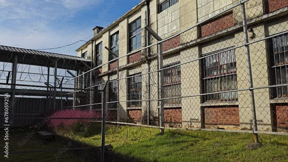 Old Prison Yard Barbed Wire Fence and Jail Building on Sunny Day Old Prison Yard Barbed Wire Fence and Jail Building on Sunny Day