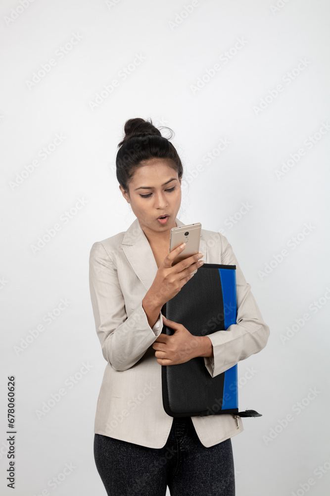 Cheerful corporate office lady holding a folder and a smartphone. Young woman in formal wear wearing white blazer against white background. Cheerful corporate office lady holding a folder and a smartphone. Young woman in formal wear wearing white blazer against white background.