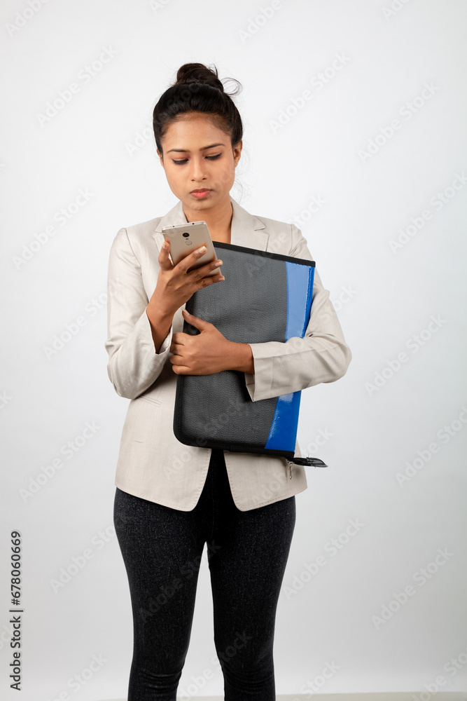 Cheerful corporate office lady holding a folder and a smartphone. Young woman in formal wear wearing white blazer against white background. Cheerful corporate office lady holding a folder and a smartphone. Young woman in formal wear wearing white blazer against white background.