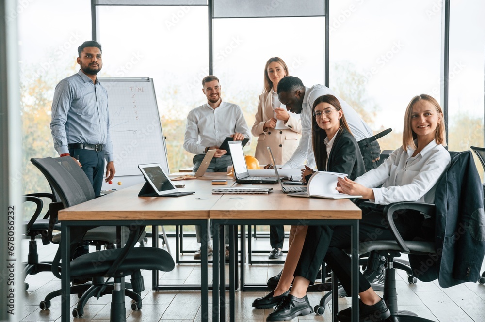 By the table and with whiteboard. Group of office workers are together indoors By the table and with whiteboard. Group of office workers are together indoors