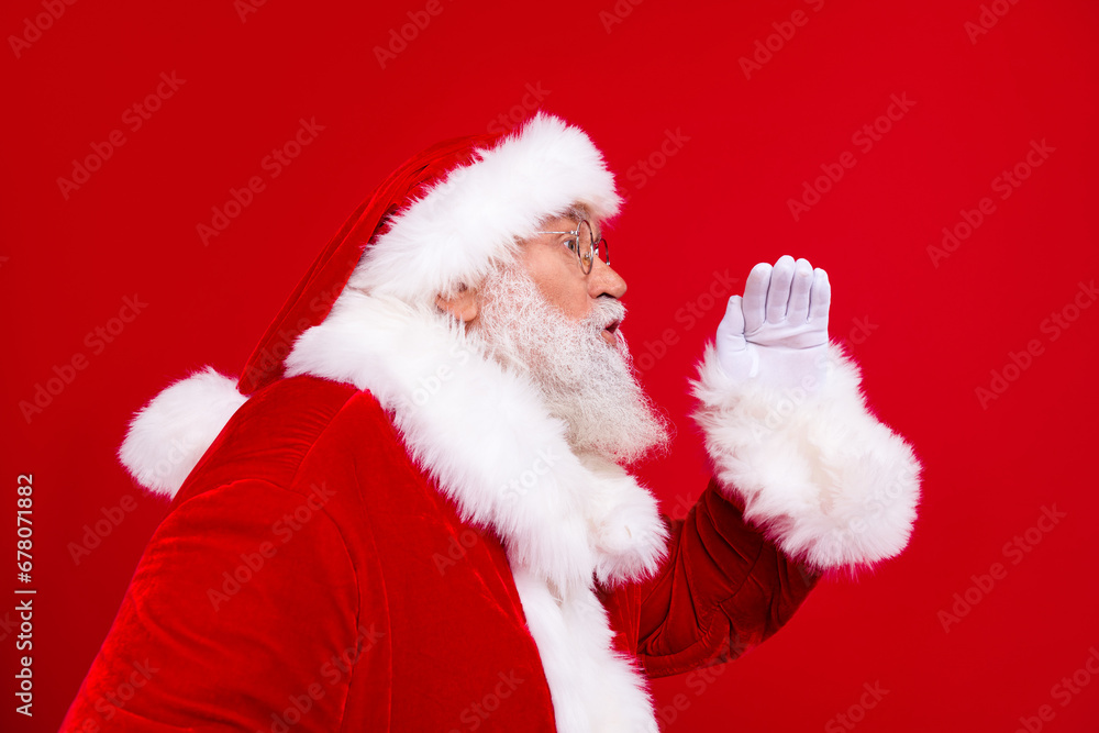 Side profile photo of excited grandfather wear stylish trendy santa costume scream in empty space isolated on red color background