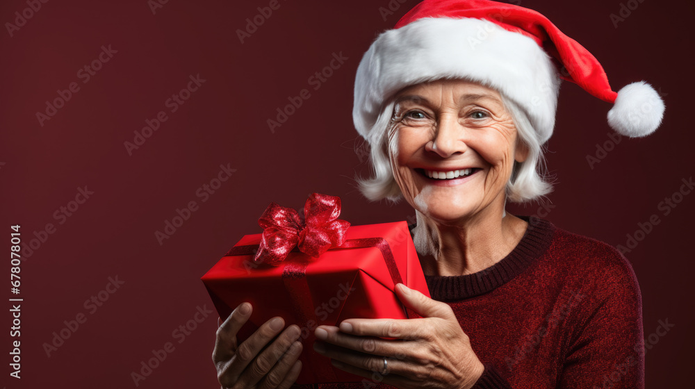 A cheerful elderly woman with white hair holding a Christmas gift with a ribbon, with a decorated Christmas tree in the background. A cheerful elderly woman with white hair holding a Christmas gift with a ribbon, with a decorated Christmas tree in the background.