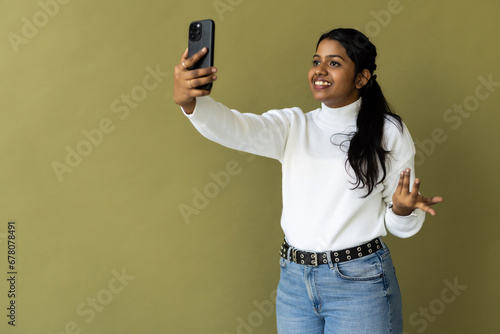 Indian woman over green background smiling and taking a selfie ready to post it on her social media. photo