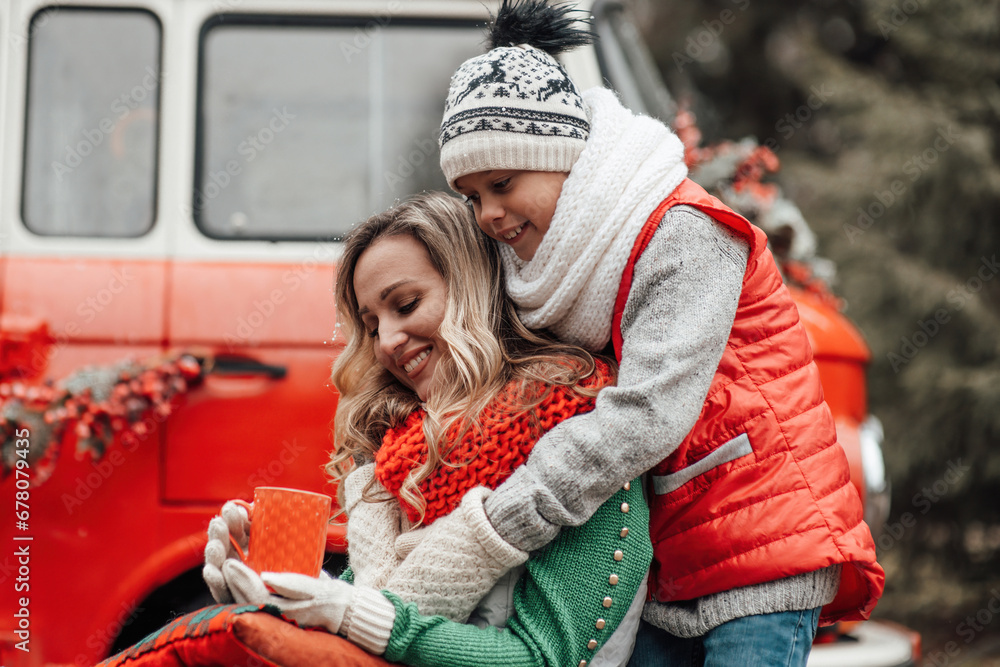 Little boy hugging his mom near Xmas old bus outdoor at Christmas Eve