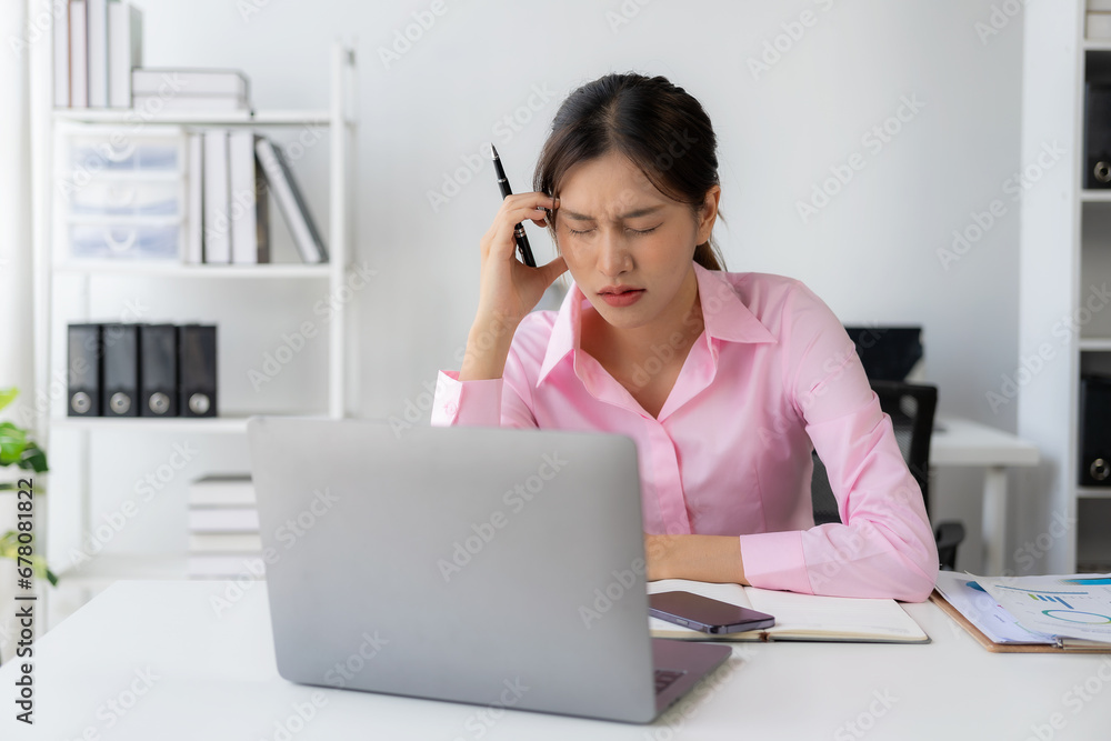 Young Asian female worker working with stress pretends to scratch her head because she is very tired working with laptop and documents on the table. Young Asian female worker working with stress pretends to scratch her head because she is very tired working with laptop and documents on the table.