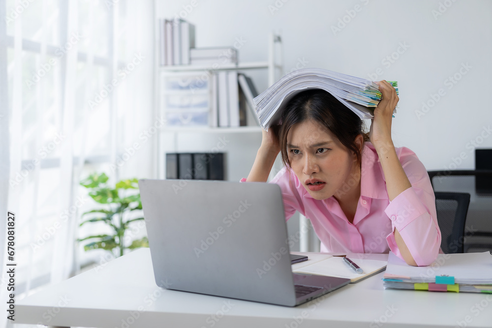 Young Asian female worker working with stress pretends to scratch her head because she is very tired working with laptop and documents on the table. Young Asian female worker working with stress pretends to scratch her head because she is very tired working with laptop and documents on the table.