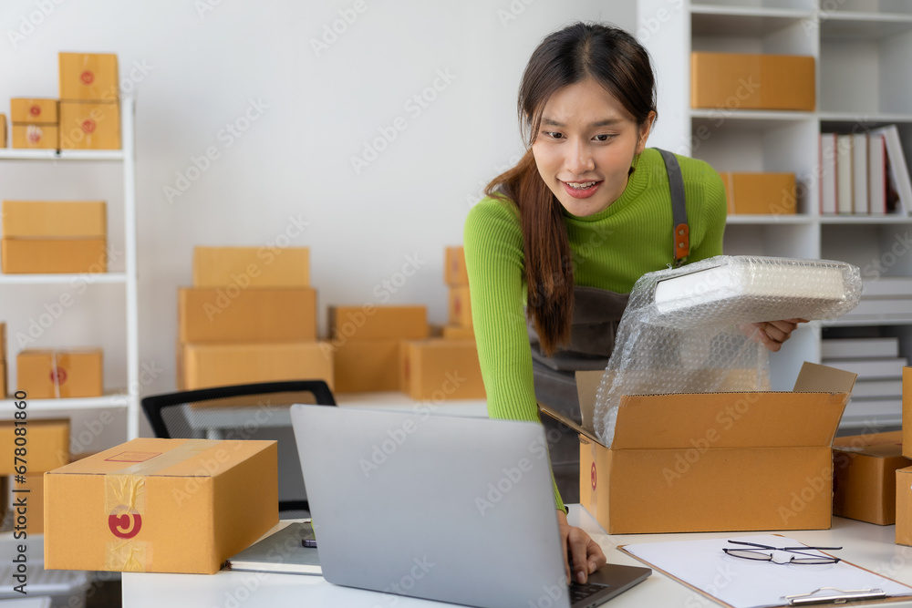 Start a small business SMEYoung Asian woman Business owner using smartphone or laptop receives and checks online orders to prepare boxes of products. Sale. Start a small business SMEYoung Asian woman Business owner using smartphone or laptop receives and checks online orders to prepare boxes of products. Sale.