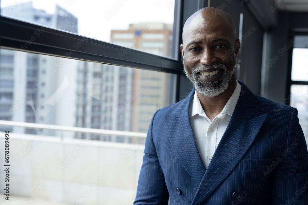Portrait of smiling senior african american businessman standing by window in office, copy space Portrait of smiling senior african american businessman standing by window in office, copy space
