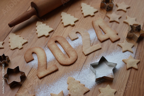 Shortcrust cookies in the form of numbers 2024 with cookie cutters and rolling pin on wooden table