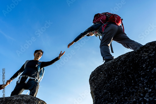Mountaineer man helping hand to hiker friend during mountaineering on the top of mountain