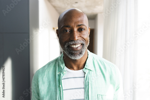 Portrait of happy bald african american mature man with beard smiling in sunny room at home photo