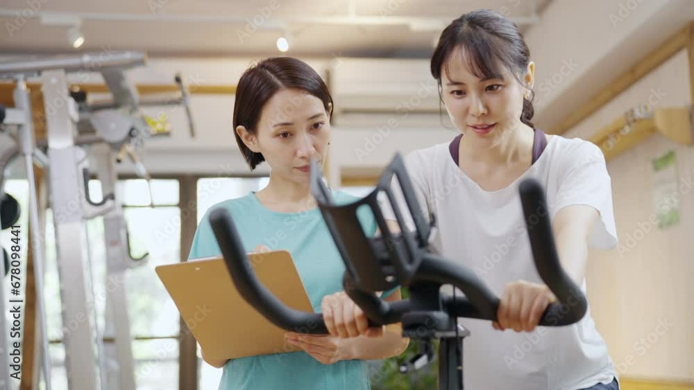 スポーツジムで運動する女性とトレーナー(エアロバイク) スポーツジムで運動する女性とトレーナー(エアロバイク)
