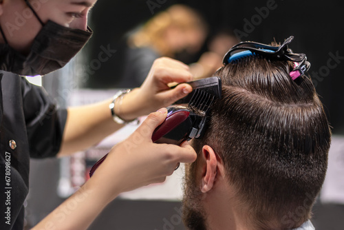 Step-by-step training in men's haircuts, combs. Female hairdresser black mask doing clipper haircut to male customer. Shaving the hair from the temples on the nozzle, parietal part is shaved, step 3