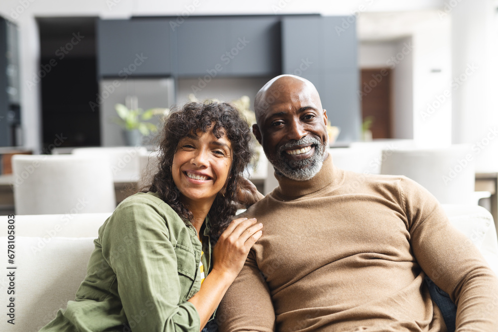 Portrait of happy diverse mature couple sitting on couch embracing in sunny living room Portrait of happy diverse mature couple sitting on couch embracing in sunny living room