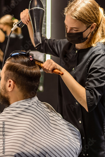 Hairdresser at work. No face, side view, close-up. Master styling men's hair with a hairdryer in a hairdresser's, step-by-step men's haircut for a young man. Hair drying