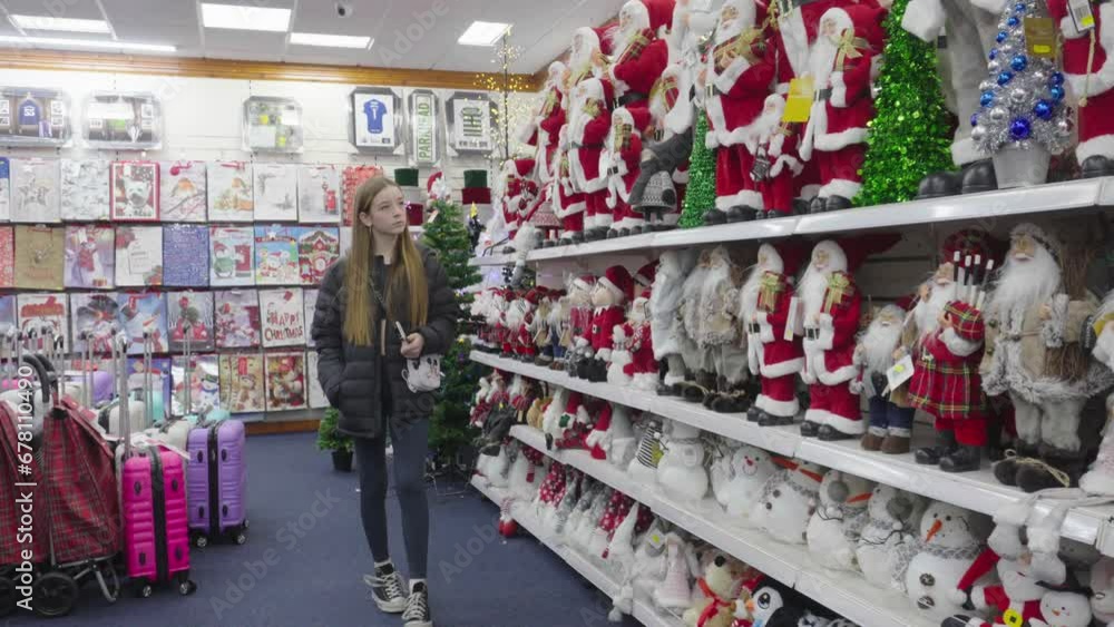 Teenage girl in Christmas section of store looking at Santa Claus dolls Teenage girl in Christmas section of store looking at Santa Claus dolls