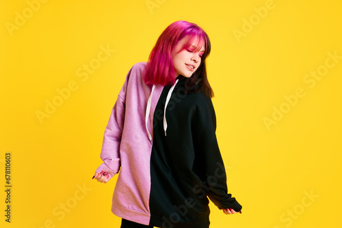 Young girl with pink eyeshadow, unusually dyed hair and piercing cheerfully dancing against vivid yellow studio background. Concept of youth, self-expression, fashion, emotions, positivity, lifestyle © master1305