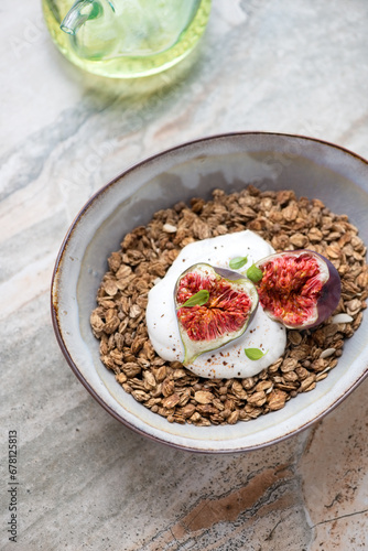 Bowl of granola served with torn figs and yogurt, vertical shot on a light-grey granite background, selective focus