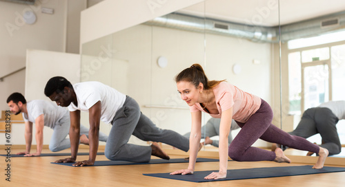Woman and men exercising on mats in gym during group fitness training.