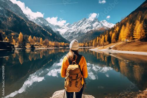 rear view of Woman with backpack admiring the sunny day in the mountains walking by the reflection lake, aesthetic look