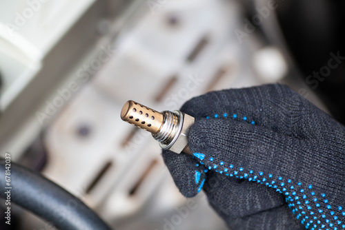 Foto Oxygen sensor for gasoline and diesel engines in the hand against car engine