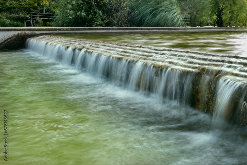 Long exposure image of a small slope with water falling into a canal in an urban park with silky type water surface