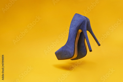 Blue velour high heel shoes floating in the air on a yellow background