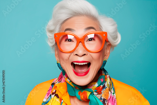 Funny stylish elderly asian grandmother in glasses poses at studio. Senior old woman looking at camera over bright background 